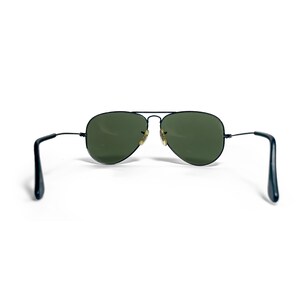 May include: Aviator sunglasses with a black metal frame and green lenses. The classic teardrop-shaped lenses are set in a thin, black frame with a double bridge. The temples are also black.