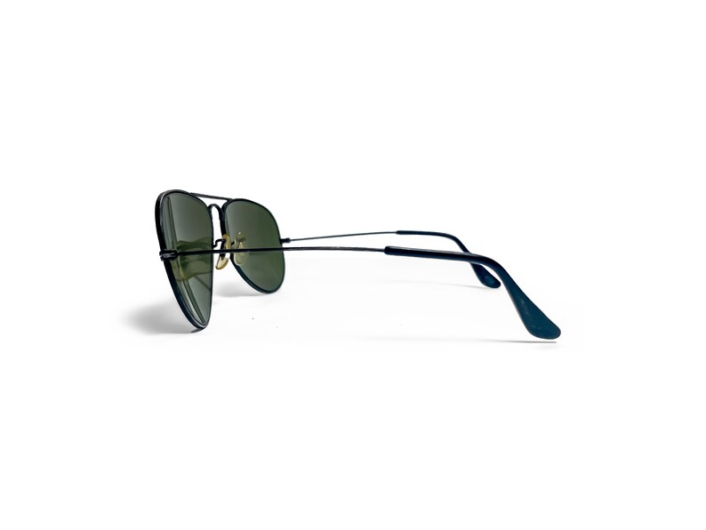 May include: Black aviator sunglasses with green lenses. The sunglasses have a double bridge and thin temples. The lenses are a teardrop shape. The frame is black and the temples curve at the ends.