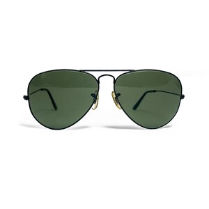 May include: Aviator-style sunglasses with a black metal frame and green lenses. The sunglasses have a double bridge and gold-colored accents on the hinges. The lenses are a teardrop shape, and the arms are thin and black.