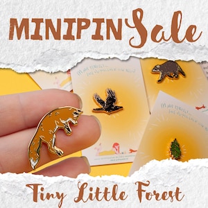 Könnte beinhalten: Eine Auswahl an Tiny Little Forest Emaille-Anstecknadeln. Die Pins zeigen einen Fuchs, einen Raben, einen Waschbären und einen kleinen Baum. Die Pins sind goldfarben mit detaillierten Emaille-Designs. Der Text "MINIPIN Sale" und "Tiny Little Forest" sind sichtbar.