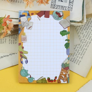 May include: A yellow notepad with a white gridded area surrounded by a border of illustrations. The illustrations include a teapot, a cup of coffee, a book, a cat, a plant, a pair of headphones, and a mug with a heart.