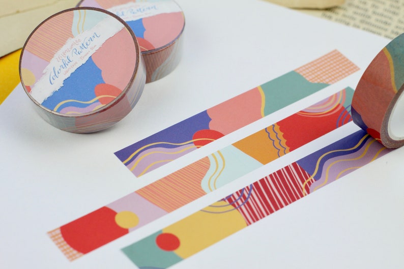 May include: Washi tape rolls with a colorful abstract pattern. The tape features a variety of shapes, lines, and colors, including red, orange, yellow, green, blue, and purple. The text on the tape reads "Happy Colorful Pattern".
