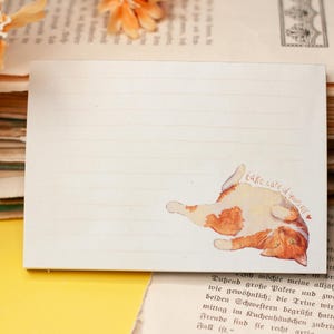 Könnte beinhalten: Ein liniertes, rechteckiges Notizbuch mit einer Aquarellillustration einer rot-weißen Katze, die auf dem Rücken liegt. Der Text "take care of yourself" steht über der Katze. Umgeben von alten Büchern und orangefarbenen Blumen.