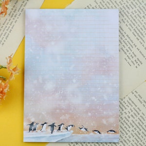 Può includere: Un blocco note rigato con uno sfondo ad acquerello di un paesaggio innevato. Un gruppo di pinguini cammina su un lastrone di ghiaccio in primo piano. Il blocco note è perfetto per scrivere lettere, appunti o tenere un diario.