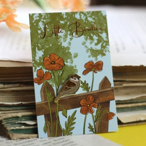 Könnte beinhalten: Dekorative Karte mit dem Text "Little Birdies", die einen braunen Vogel auf einem Holzzaun zeigt, umgeben von orangefarbenen Blumen und grünem Laub vor hellblauem Hintergrund.