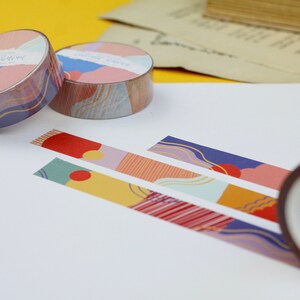 May include: Three rolls of colorful patterned washi tape with abstract designs. The tape is unrolled on a white surface, showing the different patterns. The tape is labeled "Gold Star".