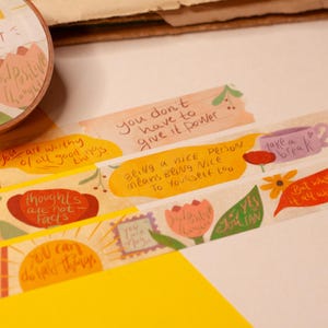 Könnte beinhalten: Dekoratives Washi-Tape und mehrere Streifen mit inspirierenden Zitaten und Illustrationen. Das Klebeband enthält Sätze wie „Du kannst schwierige Dinge tun“ und „Du bist Magie“. Die Streifen haben Blumen- und Sprechblasen-Designs.