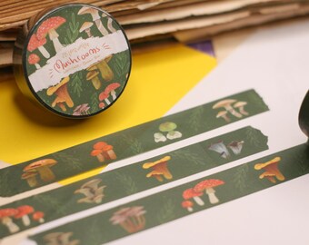 May include: A roll of decorative washi tape featuring a mushroom design with red, orange, and brown fungi on a dark green background. The tape also has the text "Mushrooms" on it. Several strips of the tape are unrolled.