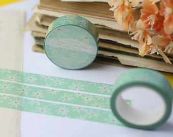 May include: Two rolls of green washi tape with a white daisy pattern and gold accents. The tape is labeled "Daily Doodles".