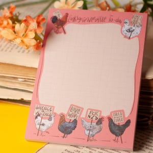 May include: A pink notepad with a grid pattern featuring illustrations of chickens holding protest signs that read Silence is Violence, Love Wins, FCK NZS, and Tired of Being Tired. The top header text reads Linksgrünversiffte To-dos.