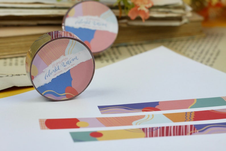 May include: A roll of washi tape with a colorful abstract pattern. The tape is labeled "Memories Colorful Pattern" and features a variety of colors, including pink, blue, yellow, and green. The tape is unrolled on a white surface, showing the pattern.