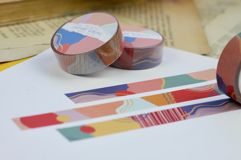 May include: Three rolls of colorful washi tape with abstract geometric patterns. The tape features a variety of colors, including blue, red, yellow, and green. The tape is labeled "Colorful Dreams".