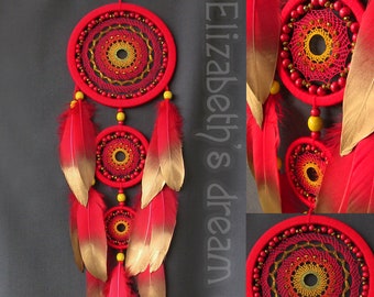 May include: Red dream catcher with gold-tipped feathers. The dream catcher features three circular woven designs with yellow and gold accents, and red beads. The text "Elizabeth's dream catchers" is visible.
