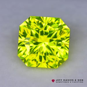 May include: A radiant, square-cut gemstone with a vibrant, chartreuse hue. The gem's facets reflect light, creating a dazzling display of brilliance. The gemstone is set against a neutral background. The logo "JEFF DAVIES & SON GEMSTONES & FACETING" is in the bottom right corner.