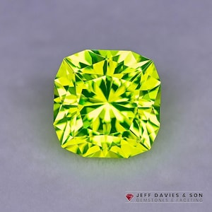 Può includere: Una gemma vibrante, taglio quadrato, con una tonalità verde lime brillante. Le sfaccettature della gemma riflettono la luce, creando un motivo a stella. La gemma è posta su uno sfondo grigio. Il testo "JEFF DAVIES & SON GEMSTONES & FACETING" è in basso.