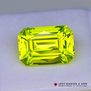 May include: A faceted, rectangular-cut, bright lime-green gemstone. The gem has a brilliant, internal glow and is set against a white background. The gem is a peridot, a popular choice for jewelry.