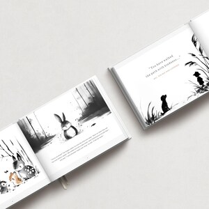 May include: Open book with black and white illustrations. One page shows a rabbit in a forest scene. Another page has a silhouette of a dog and text that reads, "You have walked the path with kindness..." The book is open on a white surface.
