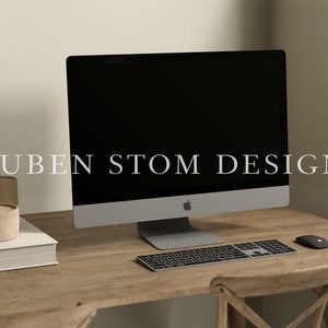 May include: A wooden desk with a silver iMac computer, a wireless keyboard, and a wireless mouse. There are two small brown decorative containers on a white book on the left side of the desk. The text "RUBEN STOM DESIGN" is visible on the computer screen.