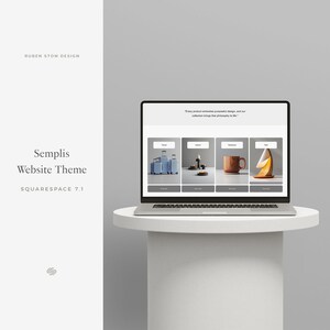 May include: A laptop computer displaying a website with the text "Every product embodies purposeful design, and our collection brings that philosophy to life." The website features four product images: a set of blue suitcases, a candle with a black base, a wooden mug, and a wooden lamp.