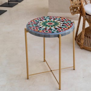 May include: A round side table with a gold metal frame and a mosaic tile top. The tile top features a colourful geometric pattern in shades of red, green, blue, and yellow.