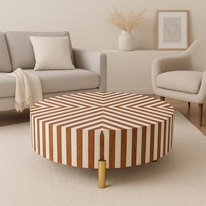 May include: A round coffee table with a brown and white striped pattern. The table has a gold-colored leg and is approximately 36 inches in diameter. The table is in a living room setting with a sofa and chairs.