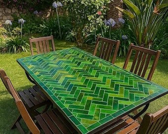 Pode incluir: Conjunto de jantar ao ar livre com uma mesa retangular com tampo de azulejos verdes em padrão espinha de peixe. A mesa é rodeada por seis cadeiras dobráveis de madeira. O conjunto está sobre relva, rodeado por vegetação e flores.