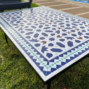 May include: A square table with a black metal frame and a white, blue, and green tiled top. The tiles feature a geometric pattern.