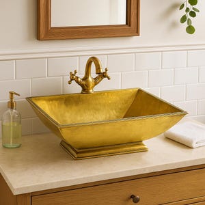 Könnte beinhalten: Ein goldfarbenes, quadratisches Badezimmerwaschbecken mit passender Armatur. Das Waschbecken hat eine gehämmerten Textur und steht auf einem erhöhten Sockel. Ein Seifenspender und ein weißes Handtuch befinden sich auf der Arbeitsplatte.