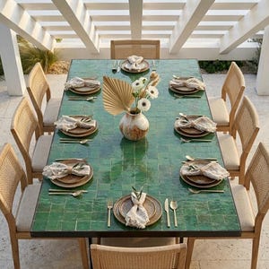 May include: A dining table set for a meal outdoors. The green tiled table is surrounded by eight woven-back chairs. Each place setting includes a plate, napkin, and silverware. A vase with flowers and a dried palm leaf decorates the center.