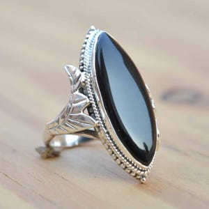 Peut inclure: Une bague en argent avec une pierre ovale noire et un motif de feuille sur le côté.