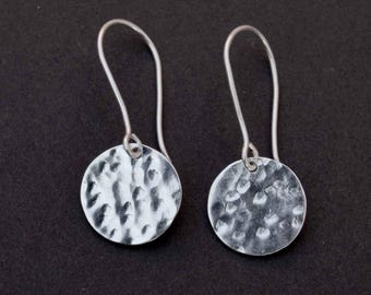 May include: A pair of silver dangle earrings with hammered round disc charms. The earrings have a simple, minimalist design.