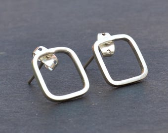 May include: A pair of silver square stud earrings with a simple, minimalist design. The earrings are made of a thin metal wire and have a slightly rounded edge.