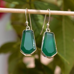 Puede incluir: Un par de pendientes de plata con gotas de piedras preciosas verdes. Las piedras preciosas son facetadas y tienen una forma geométrica.