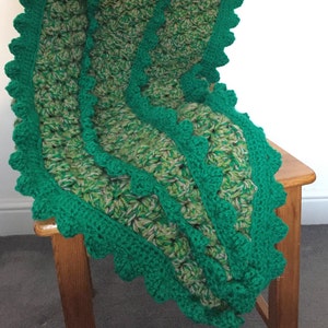 May include: A green and brown crocheted blanket with a scalloped edge. The blanket is draped over a wooden chair.