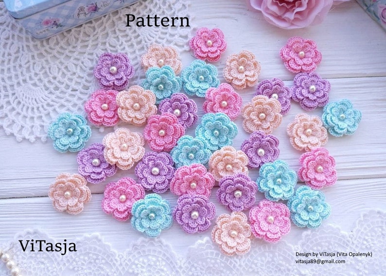 May include: A collection of crocheted flower appliques in various pastel colors, including pink, blue, purple, and peach. Each flower has a pearl bead center. The word "Pattern" is visible in the image.