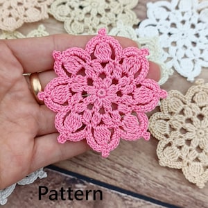 Könnte beinhalten: Eine rosa gehäkelte Blume mit einem zarten Muster. Die Blume ist umgeben von anderen gehäkelten Blumen in verschiedenen Farben.