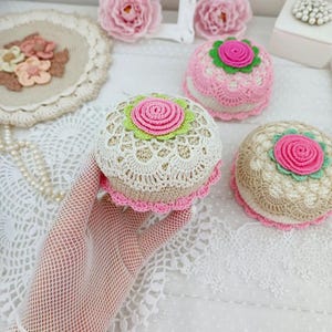 Può includere: Tre oggetti decorativi all'uncinetto di forma rotonda con base beige, uno strato superiore in pizzo bianco e una rosa centrale rosa circondata da un bordo verde chiaro. Ogni pezzo è rifinito con un bordo smerlato rosa.
