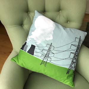 May include: A green and blue cushion with a black and white illustration of a power station and power lines. The power station is emitting smoke.