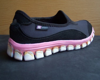 May include: Black slip-on shoe with a pink and white sole. The sole has a unique design with multiple rows of teeth.