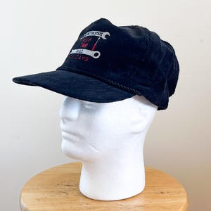 Könnte beinhalten: Schwarze Cord-Baseballkappe mit gebogenem Schirm. Die Kappe hat gestickten Text und Grafiken in Weiß und Rot, darunter die Worte "Washington State" und "Rat Days". Ein schwarzes Seildetail ziert die Rückseite.