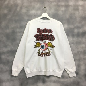 May include: White sweatshirt with a graphic print of a winged eye with a red iris and a yellow pupil. The text "System Von Dutch Lives" is printed above the eye.