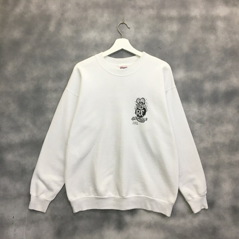 May include: White sweatshirt with a black and white graphic of a cartoon rat with the text "Rat Fink" on a circle. The sweatshirt has a crew neck and long sleeves.