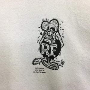 May include: Black and white illustration of a cartoon rat with the text "RF" in a circle. The text "Rat Fink TM Ed Roth '84 Lic. Dist. Tamarete" is below the illustration.
