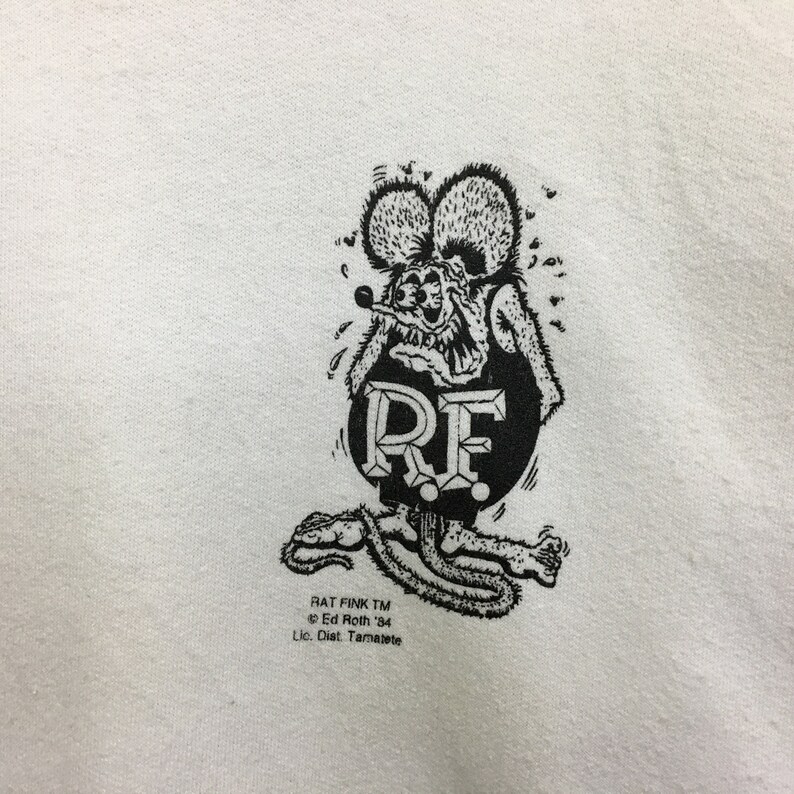 May include: Black and white illustration of a cartoon rat with the text "RF" in a circle. The text "Rat Fink TM Ed Roth '84 Lic. Dist. Tamarete" is below the illustration.