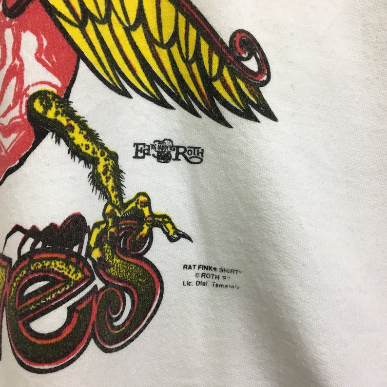 May include: White t-shirt with a red, yellow, and black graphic of a bird with the text "Rat Fink Shirts" and "Roth '93" printed below the graphic.
