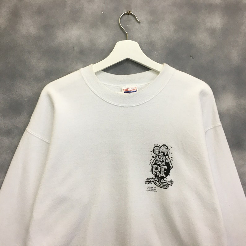 May include: White sweatshirt with a black and white graphic of a cartoon rat with the text "Rat Fink" and "Ed "Big Daddy" Roth" on the front.