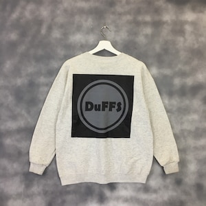 May include: A gray sweatshirt with a black square on the back. The square has a gray circle with the word "DUFFS" in black letters.