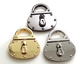 May include: Three metal handbag lock charms in different finishes: silver, gold, and black. Each charm features a detailed padlock design with a keyhole and a decorative knob.