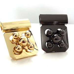 May include: Two metal clasps with a decorative design. One clasp is gold and the other is black.