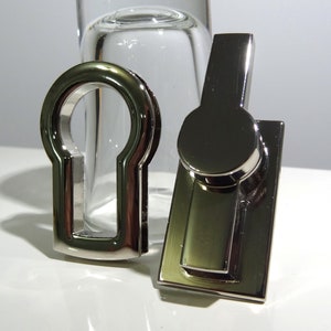 May include: Two silver-toned metal keyhole covers. One is a simple keyhole cover, the other is a rectangular cover with a round keyhole cover on top.